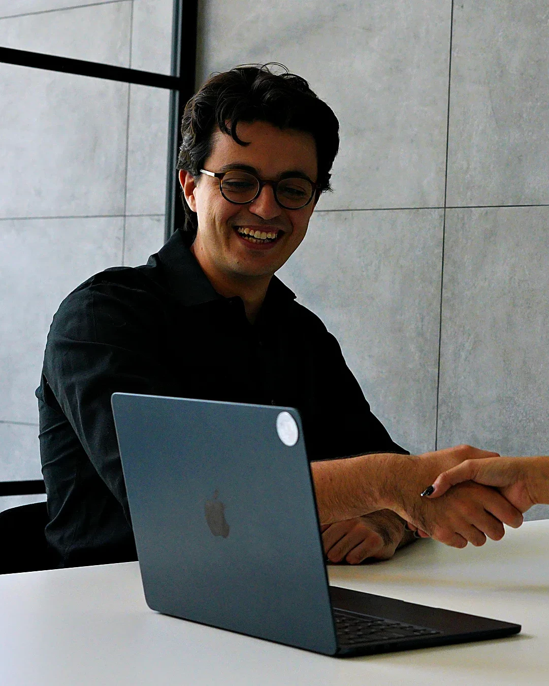 El equipo de Button Up Media cerrando un proyecto con un apretón de manos sobre la laptop