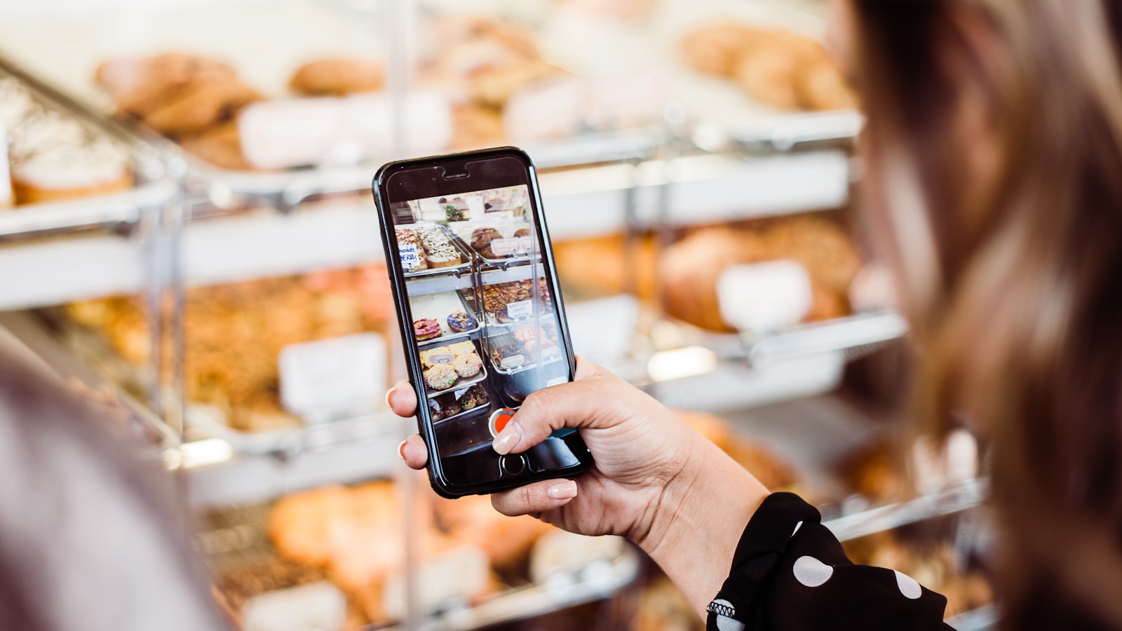 A woman photographing a bakery display case with her phone at an American restaurant