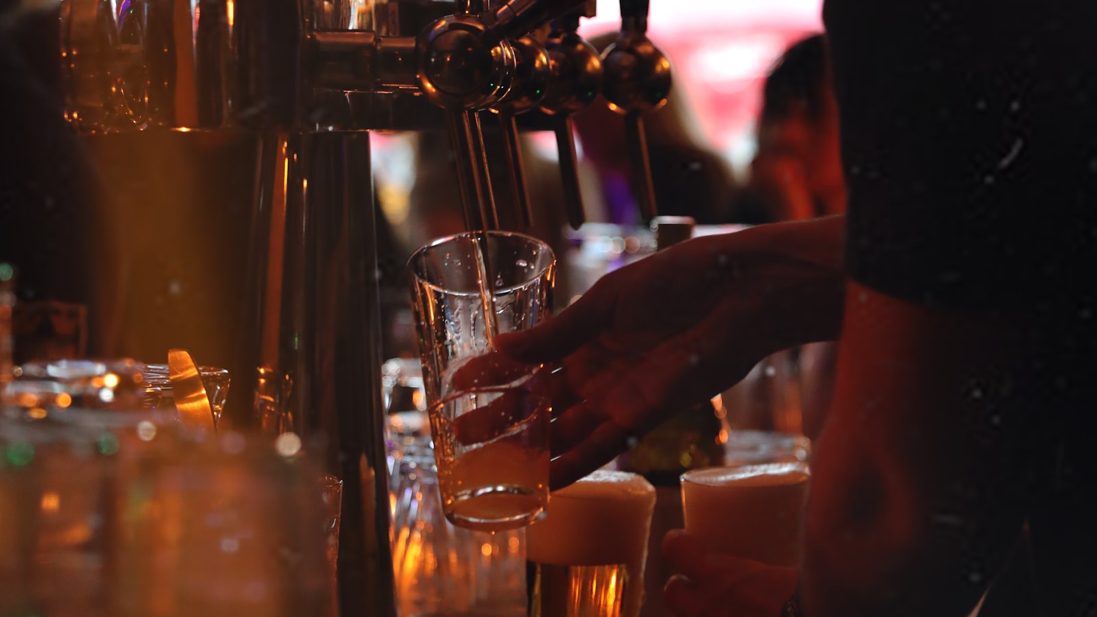 A bartender pouring beer from the taps at a busy, warmly lit American bar at night