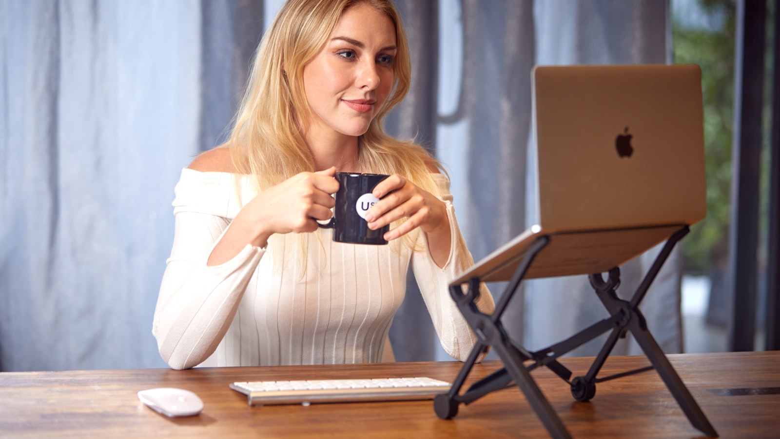 A person at a cafe table looking something up on a laptop while holding a cup of coffee