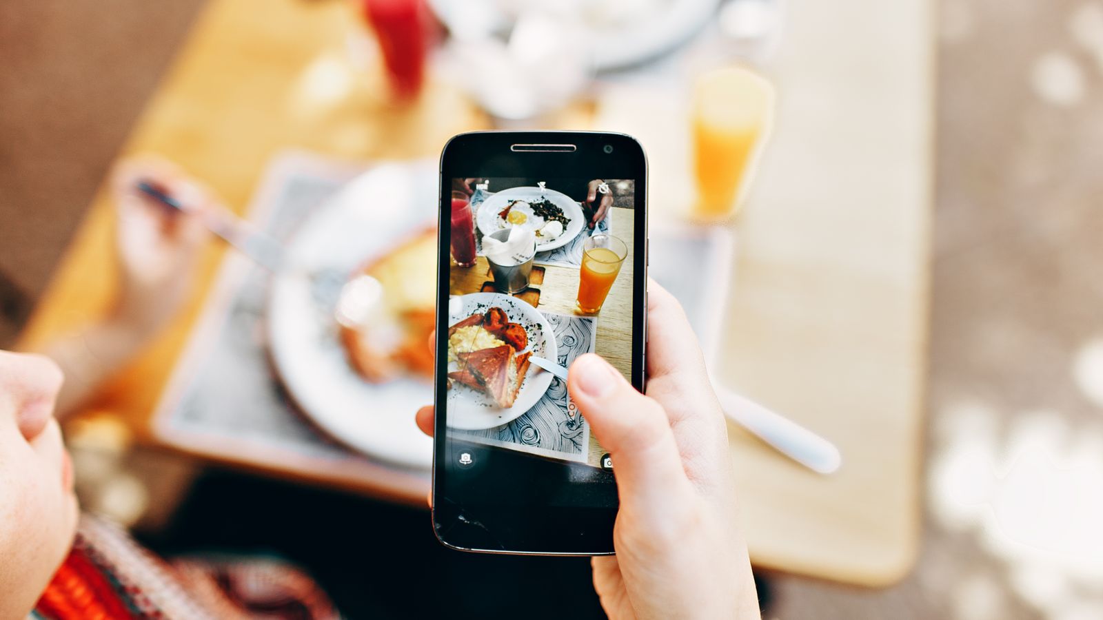 A person filming a plate of food with a phone at a restaurant table