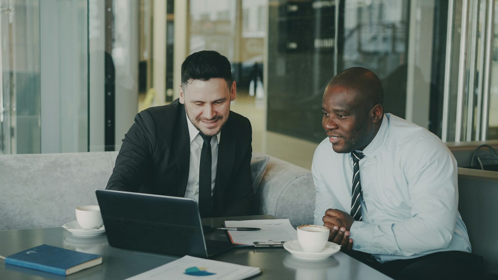 Two professionals reviewing a laptop together at a table over coffee