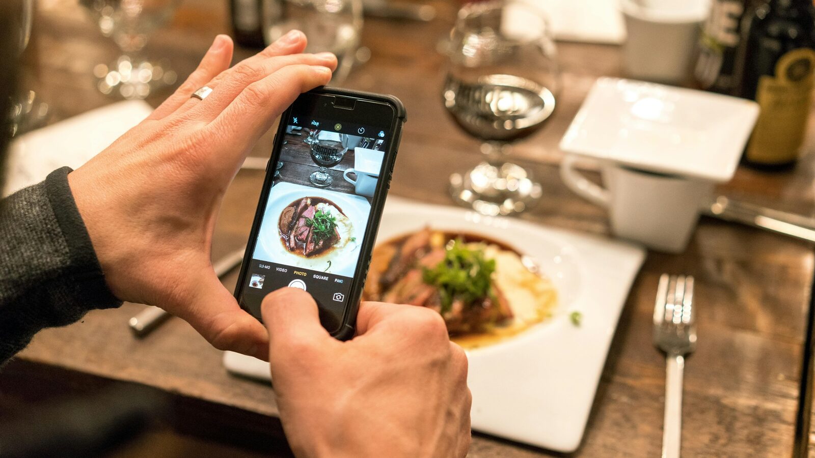A person photographing a plated dish with a phone at a restaurant table